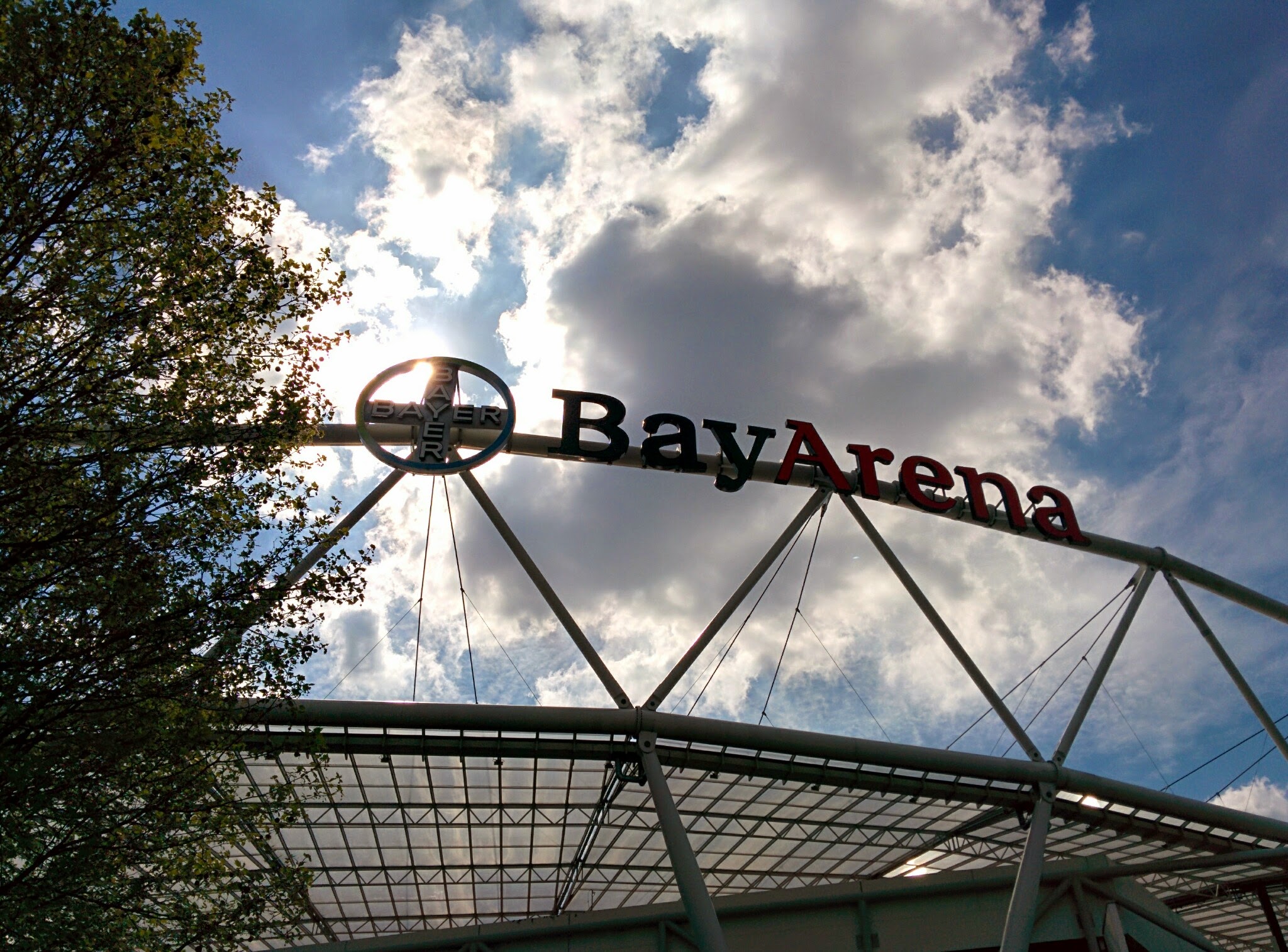 Der Schriftzug BayArena ist am Stadion zu sehen. Im Hinergrund sieht man einen sonnigen, leichtblauen Himmel.