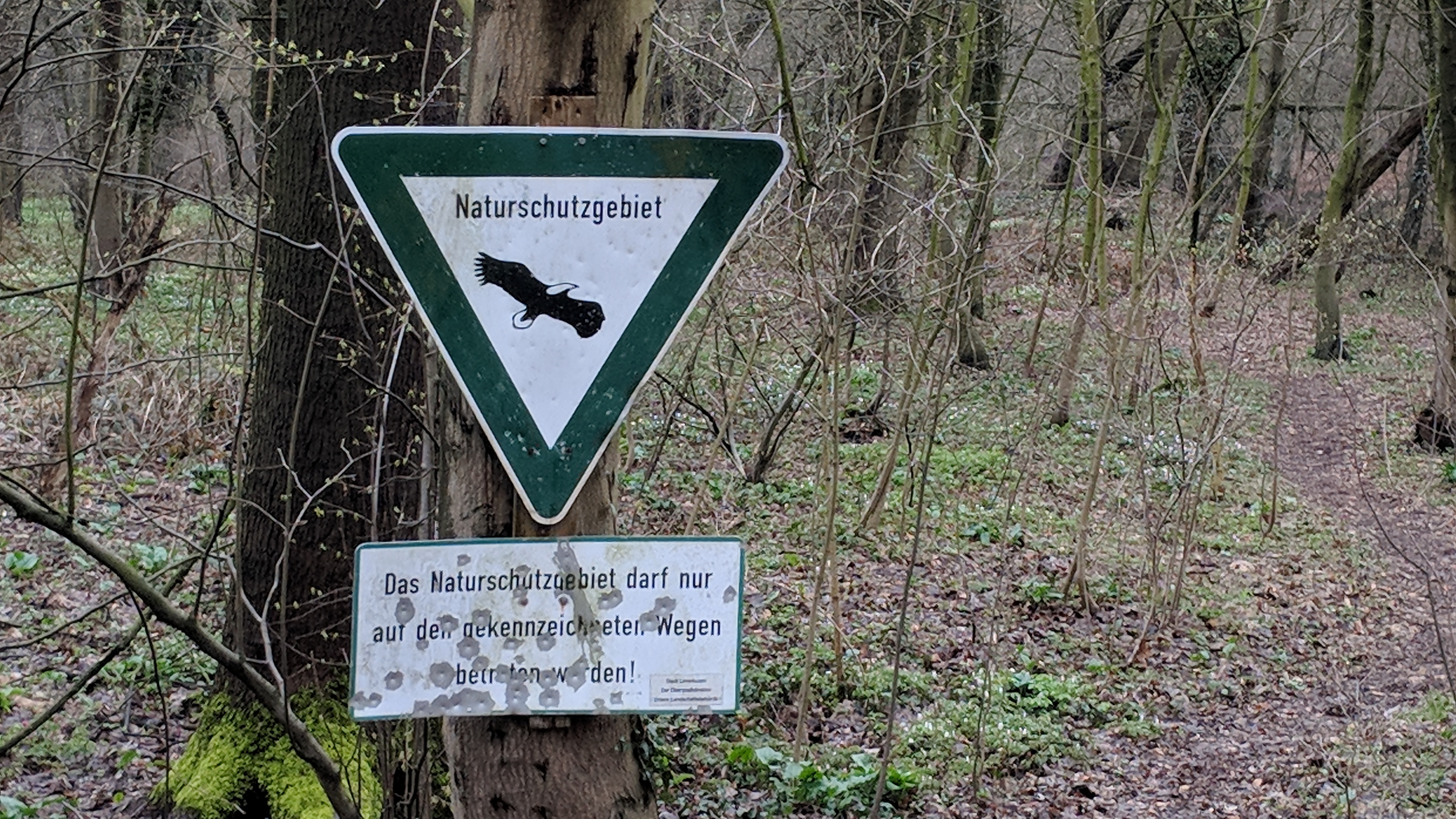 An einem Pfahl ist das Schuld Naturschutzgebiet angebracht. Darunter steht: "Das Naturschutzgebiet darf nur auf den gekennzeichneten Wegen betreten werden. Stadt Leverkusen. Der Oberbürgermeister."