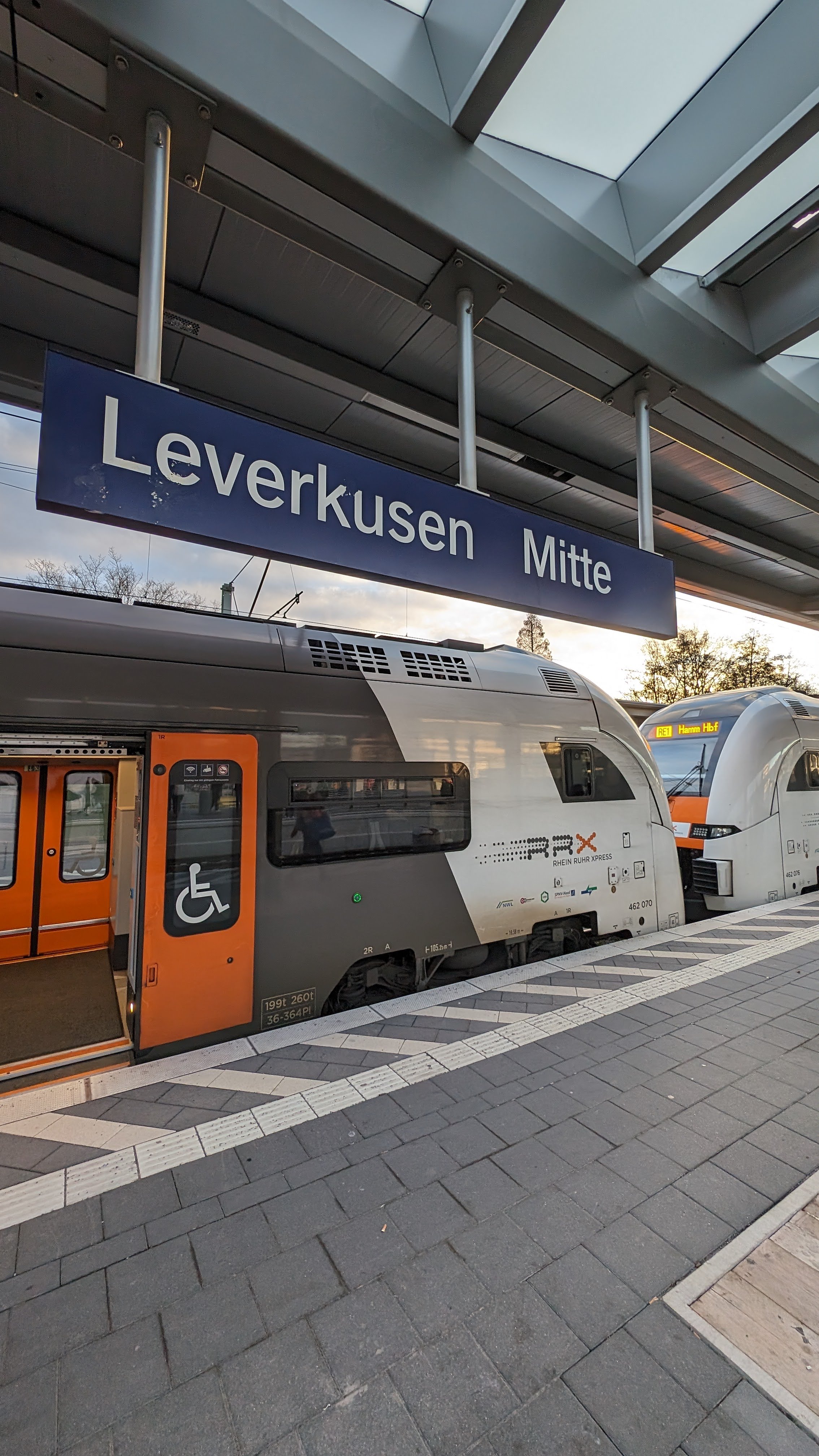 Ein RRX am Bahnsteig in Leverkusen Mitte. Davor ein Bahnhofsschild mit der Aufschrift "Leverkusen Mitte".